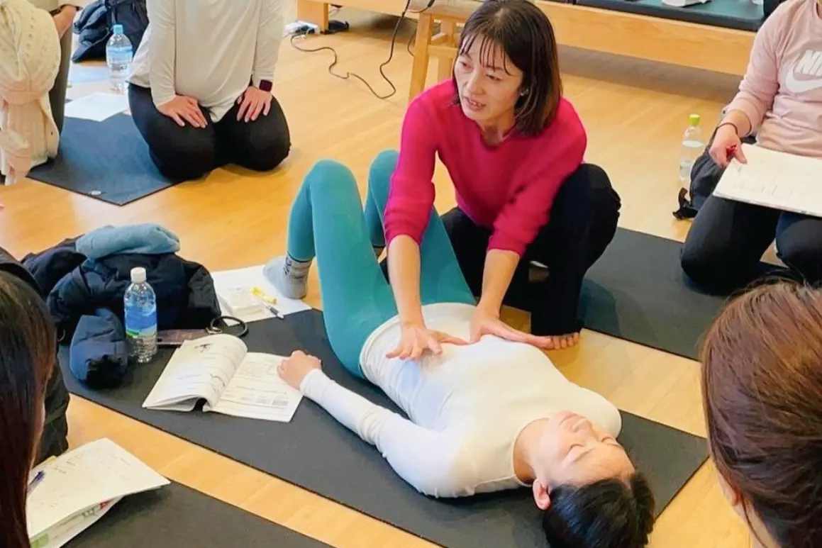 講師が仰向けの受講生に手技をデモンストレーションし、受講生が見学している様子