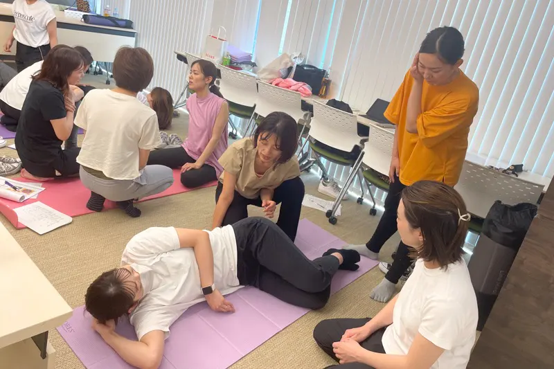 講師が横向きに寝た受講生へ手技を指導し、受講生が見学している様子